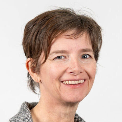 Sandra Berendsen van SAMEN Geldrop-Mierlo lacht naar de camera, draagt een grijs colbert en staat voor een lichte achtergrond.