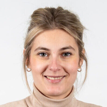 Jonge vrouw met lichtbruin haar in staart, beige coltrui en oorringen lacht naar de camera in Geldrop-Mierlo.